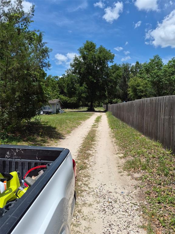 A dirt driveway leads toward a small shed and trees beside a wooden fence — 11366 SE 40TH AVENUE, BELLEVIEW, FL