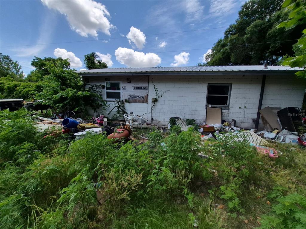 The exterior of a weathered, single-story concrete block house surrounded by overgrown vegetation and debris — 11366 SE 40TH AVENUE, BELLEVIEW, FL
