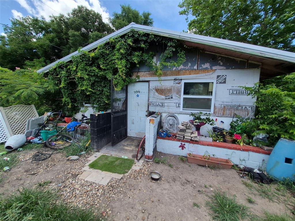 The exterior of a small, weathered house features exposed insulation panels and overgrown vegetation — 11366 SE 40TH AVENUE, BELLEVIEW, FL
