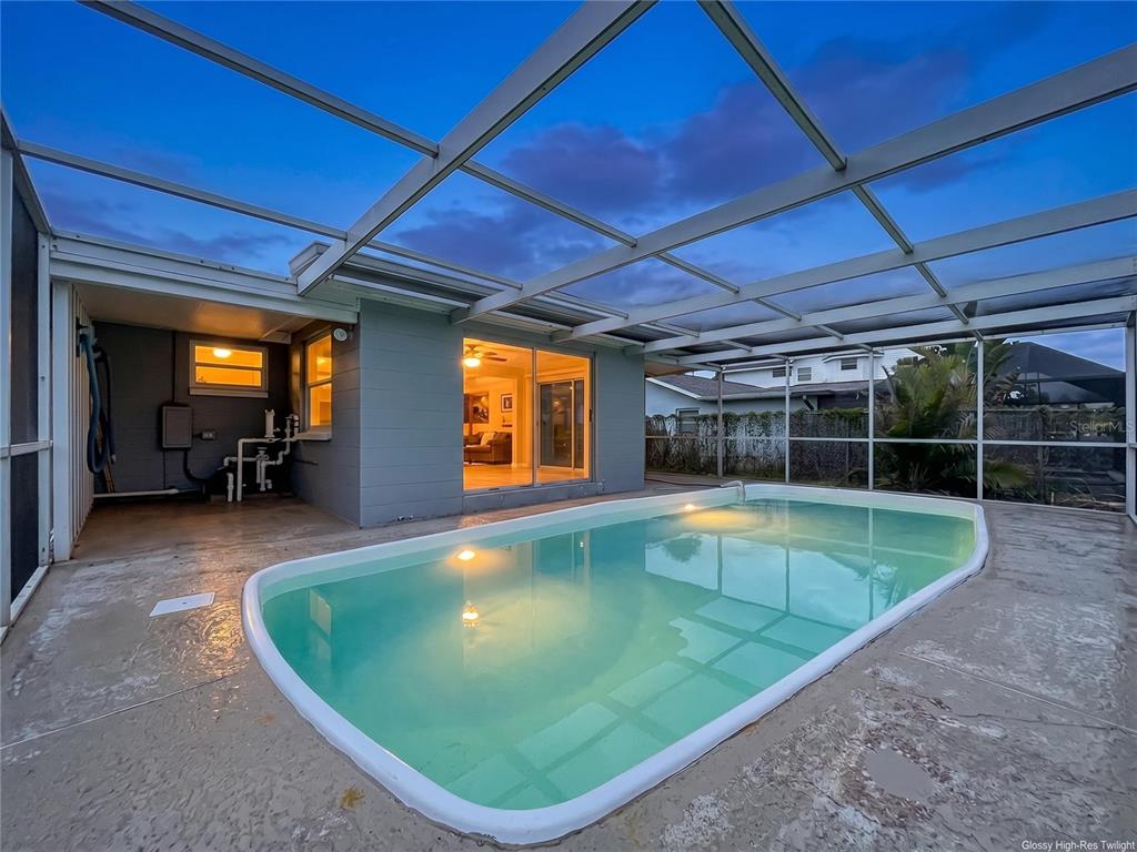 An outdoor swimming pool enclosed by a screened lanai attached to a gray house — 7513 HATTERAS DRIVE, HUDSON, FL