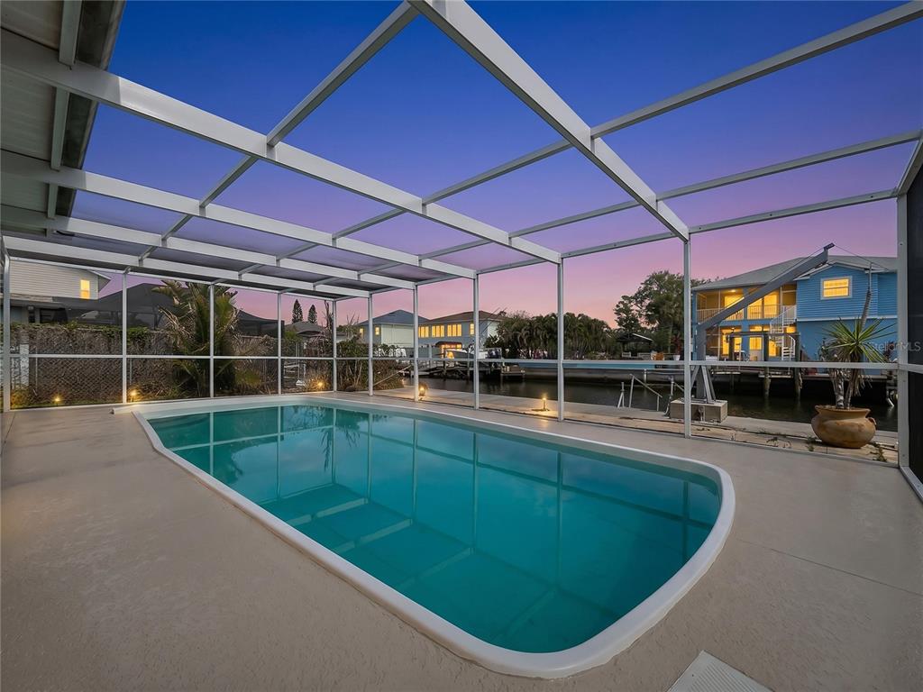 A screened-in swimming pool patio overlooks a canal at sunset — 7513 HATTERAS DRIVE, HUDSON, FL