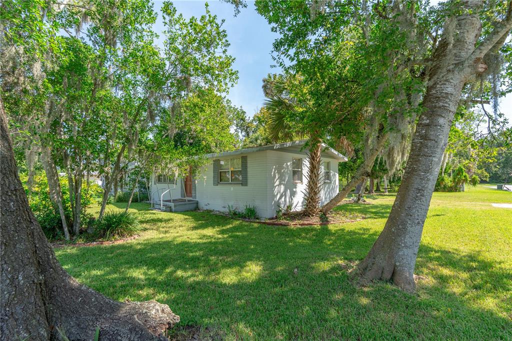 A single-story white house sits on a grassy lot surrounded by large, moss-covered trees — 553 S LANVALE AVENUE, DAYTONA BEACH, FL