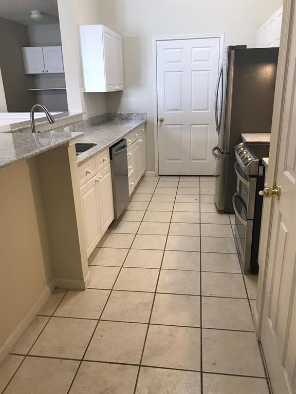 A kitchen features white cabinets, granite countertops, stainless steel appliances, and light-colored tile flooring — 239 LONGVIEW AVENUE UNIT 201, CELEBRATION, FL