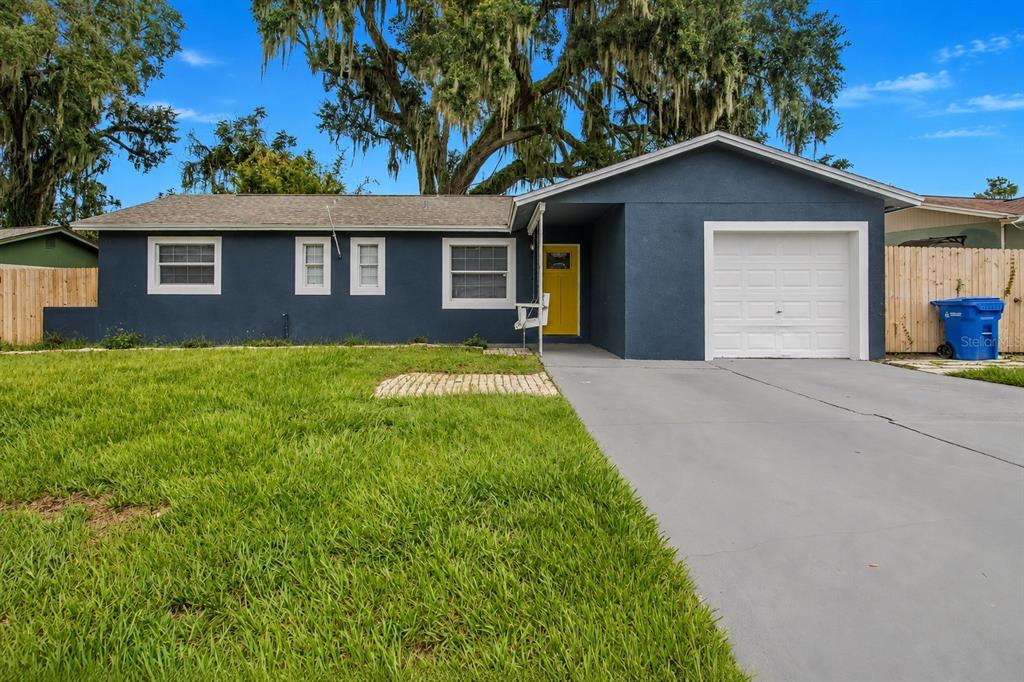 A single-story house with dark blue siding, a yellow front door, and a concrete driveway — 113 INWOOD CIRCLE, BRANDON, FL