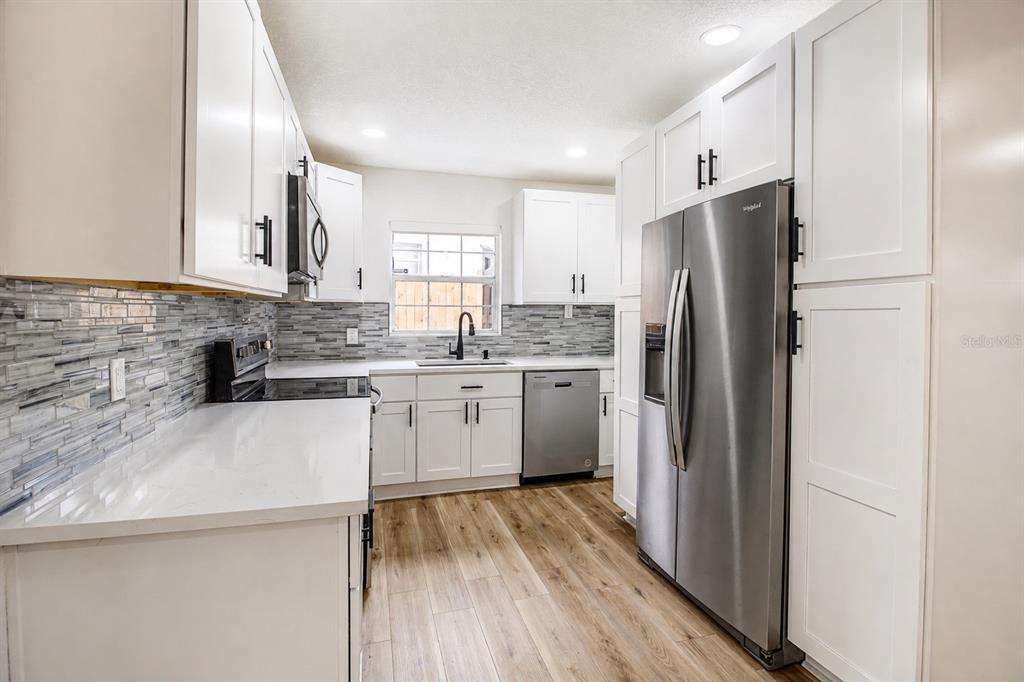 A kitchen with white cabinets, stainless steel appliances, quartz countertops, and a glass tile backsplash — 113 INWOOD CIRCLE, BRANDON, FL