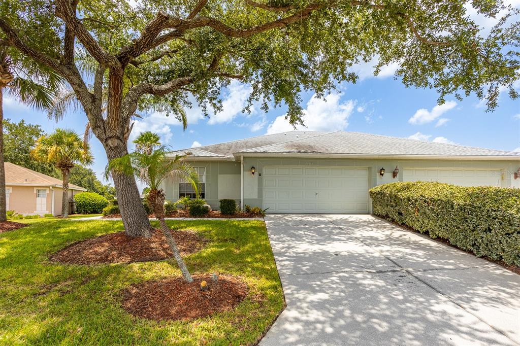 A light green house with a two-car garage, a concrete driveway, and large shade trees — 29312 MARKER LOOP, SAN ANTONIO, FL