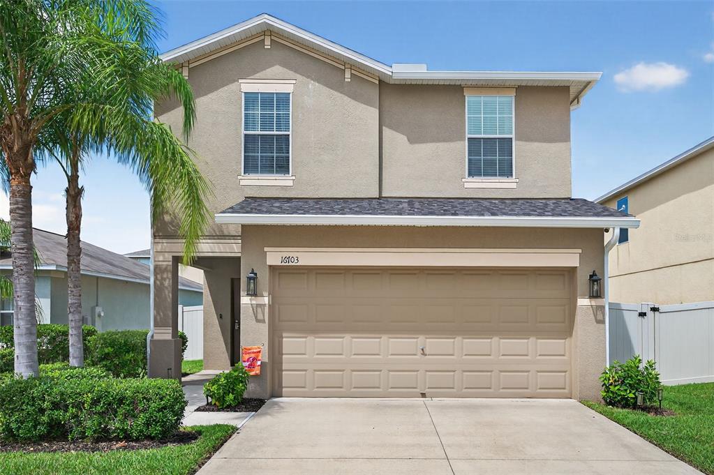 A two-story suburban house features a tan stucco exterior, a two-car garage, and palm trees — 16703 MYRTLE SAND DR, WIMAUMA, FL