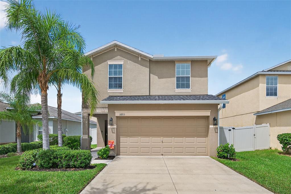 A two-story suburban house features a tan stucco exterior, a two-car garage, and a palm tree — 16703 MYRTLE SAND DR, WIMAUMA, FL