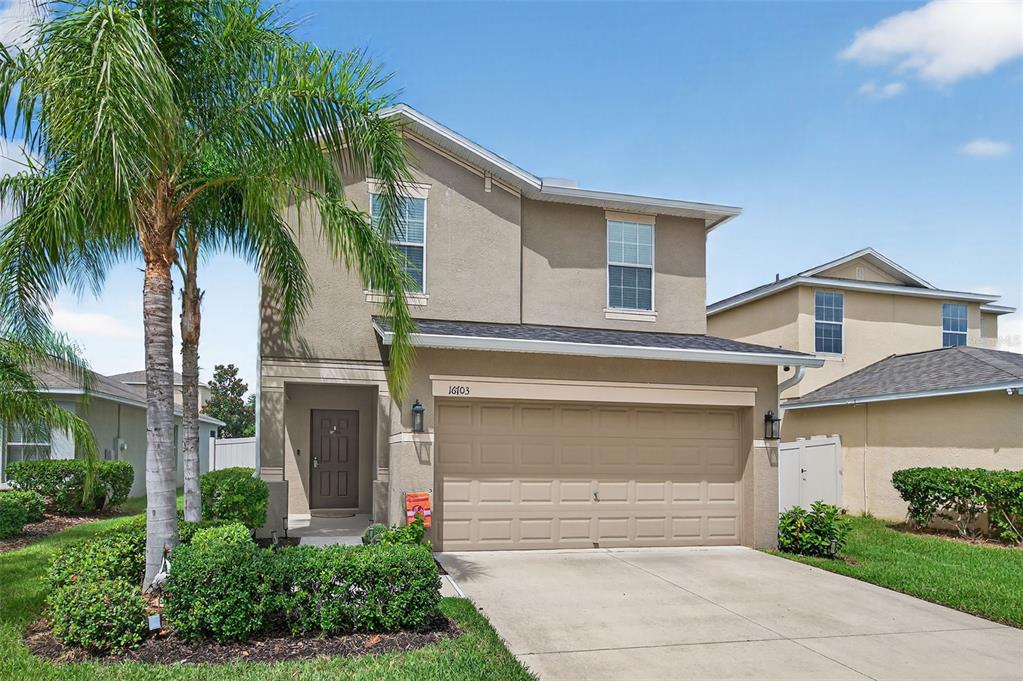 A two-story suburban house with a tan stucco exterior, a two-car garage, and a palm tree — 16703 MYRTLE SAND DR, WIMAUMA, FL
