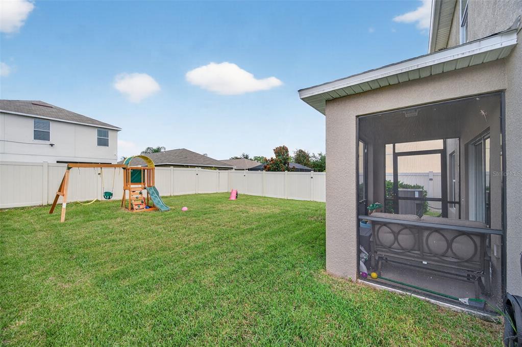 A backyard features a grassy lawn, a wooden playset, and a screened-in patio area — 16703 MYRTLE SAND DR, WIMAUMA, FL