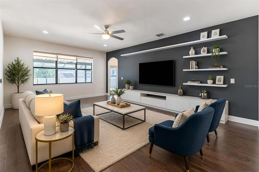 A living room features a dark accent wall with floating shelves, a television, and furniture — 5728 RUE GALILEE LANE, SANFORD, FL