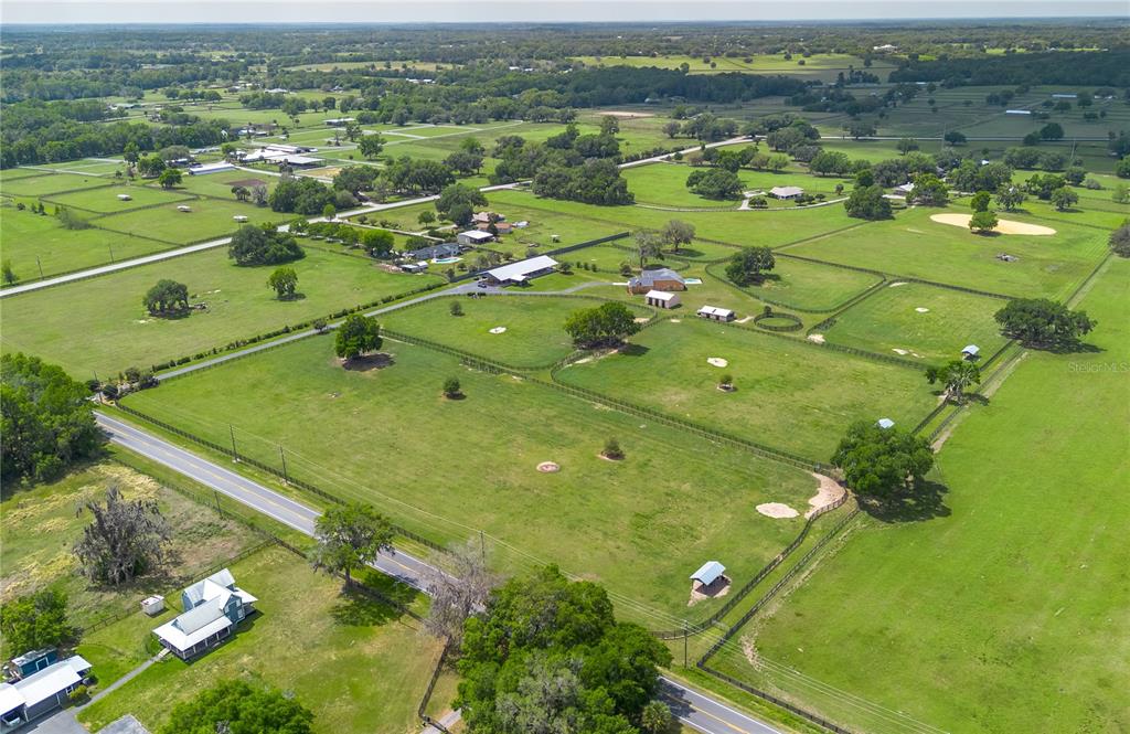An aerial view shows a rural property with fenced pastures, several buildings, and a road — 12610 NW GAINESVILLE ROAD, REDDICK, FL