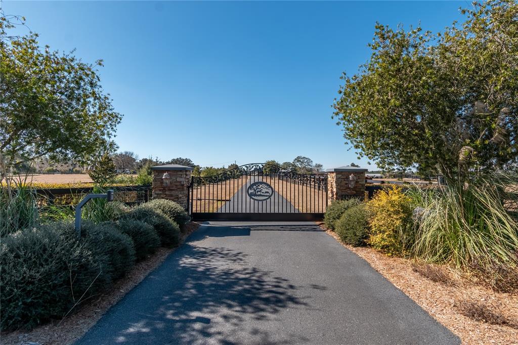 A paved driveway leads to a decorative metal gate flanked by stone pillars and landscaping — 12610 NW GAINESVILLE ROAD, REDDICK, FL