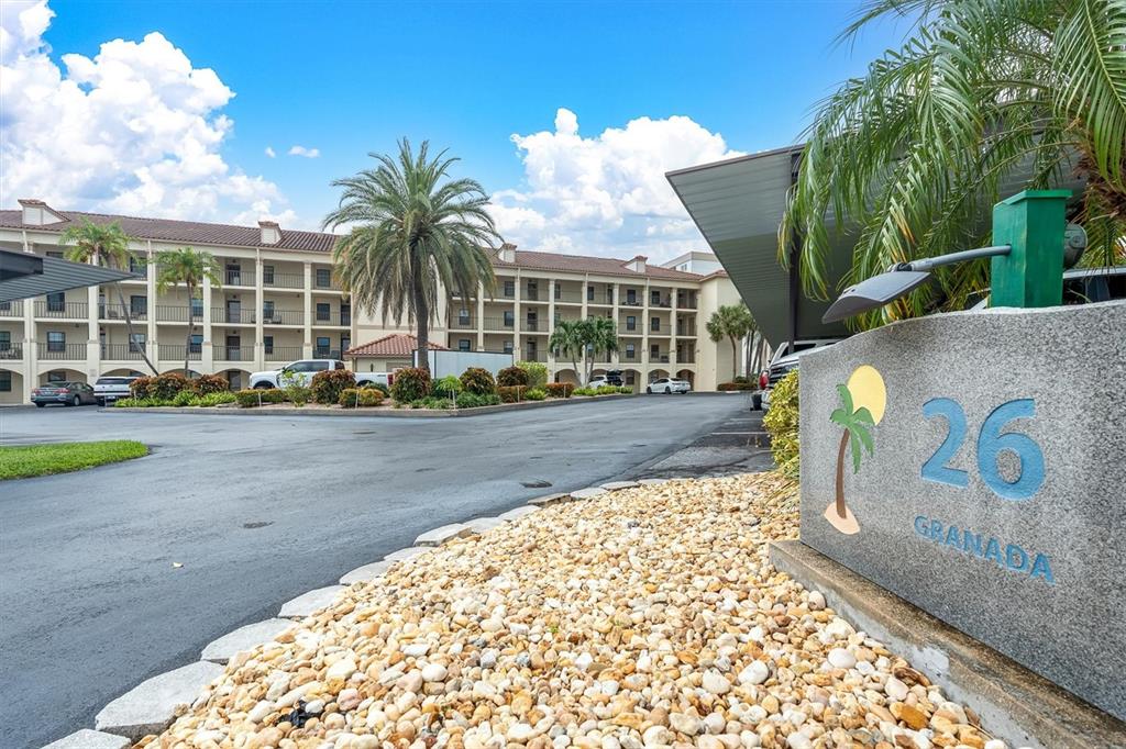 A multi-story apartment building with a parking lot and palm trees under a blue sky — 19029 US HIGHWAY 19 N UNIT 26-208, CLEARWATER, FL