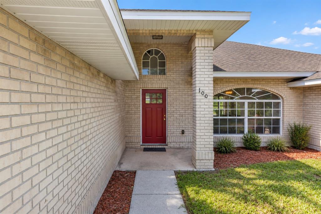 A brick house exterior features a red front door, a concrete walkway, and arched windows — 1005 WHISPRING CREEK WAY, OSTEEN, FL