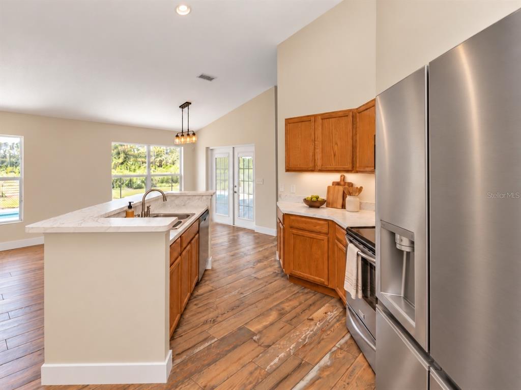 An open-concept living room and kitchen featuring wood-look flooring, a fireplace, and vaulted ceilings — 1005 WHISPRING CREEK WAY, OSTEEN, FL