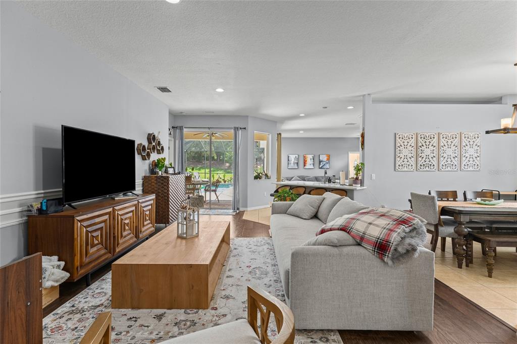 A living room features a grey sofa, wooden coffee table, media console, and dining area — 14229 CATTLE EGRET PLACE, LAKEWOOD RANCH, FL