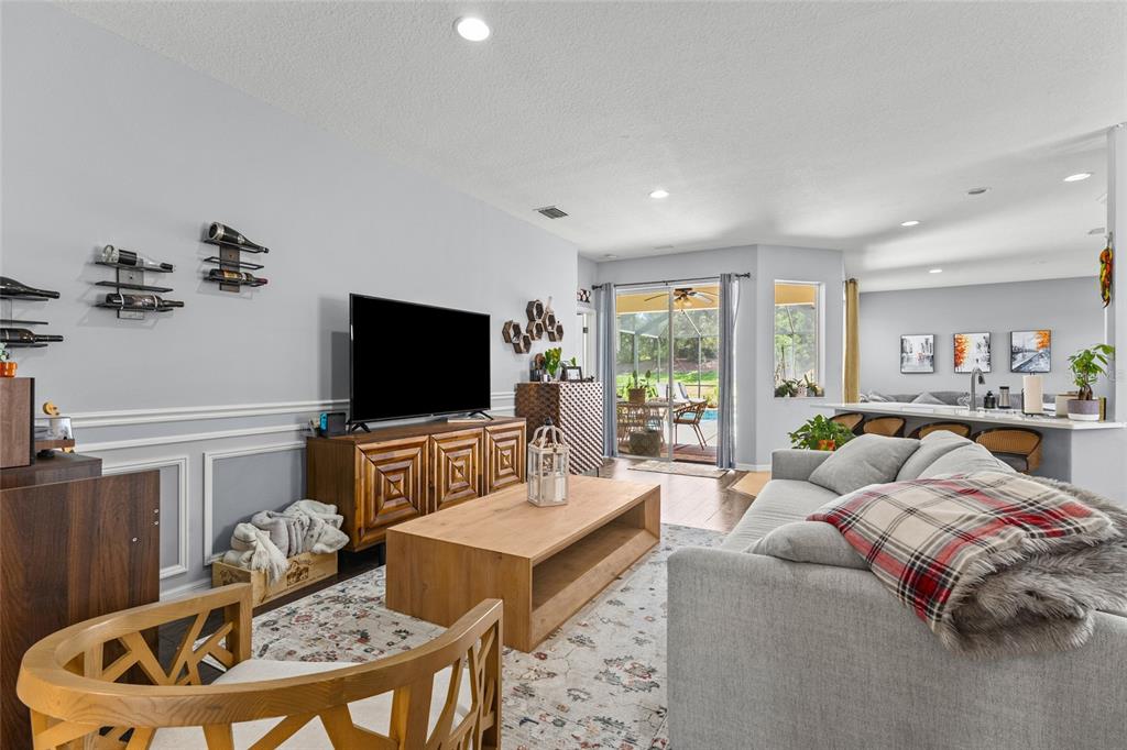 A living room features a grey sofa, wooden coffee table, television, and a sliding glass door — 14229 CATTLE EGRET PLACE, LAKEWOOD RANCH, FL