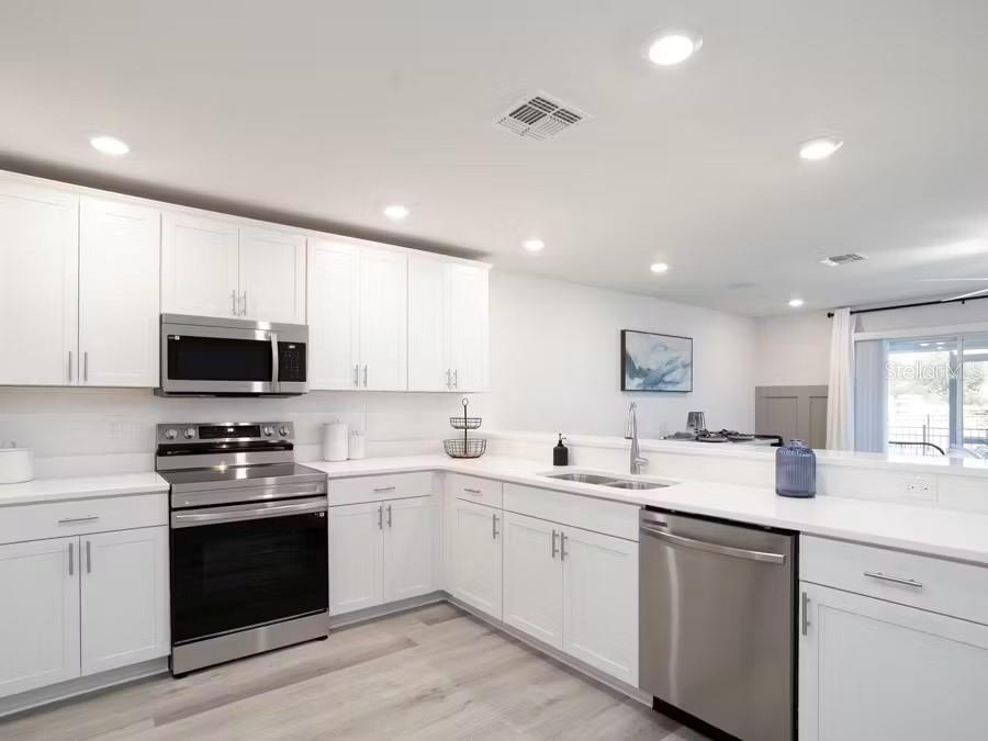 A modern kitchen features white cabinets, stainless steel appliances, and light wood-look flooring — 394 CHESAPEAKE DRIVE, ST CLOUD, FL