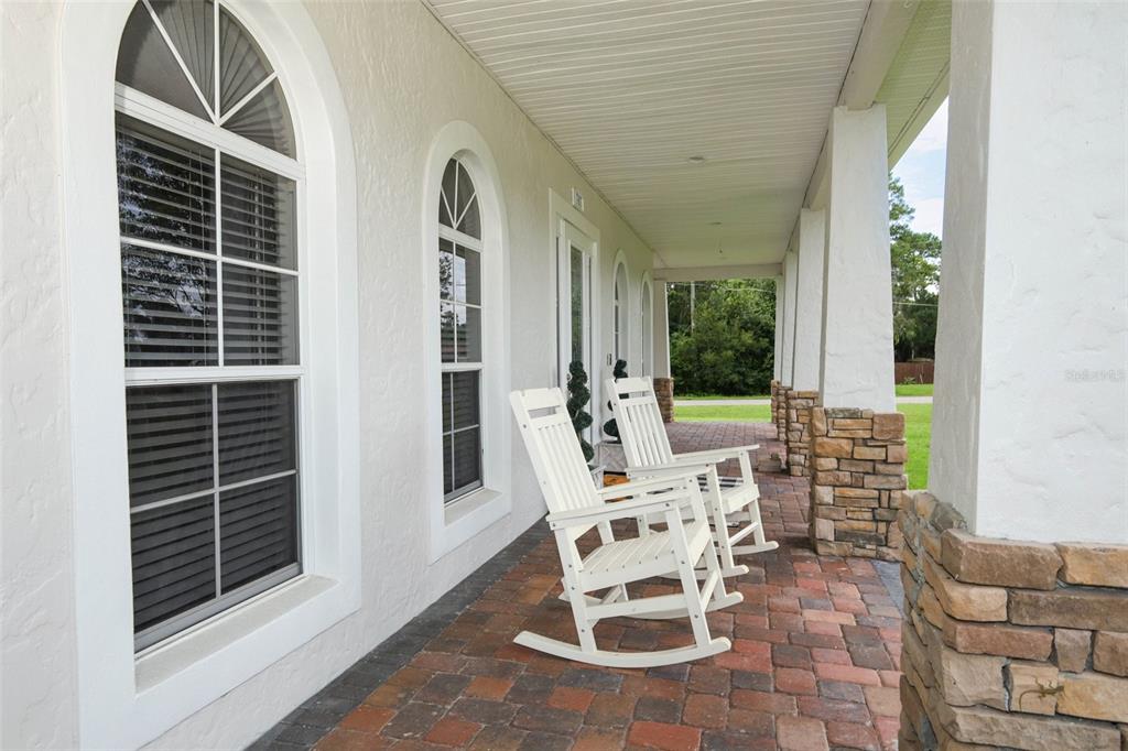 A covered porch features a brick floor, white columns with stone bases, and two rocking chairs — 787 FANTASY LANE, CHULUOTA, FL