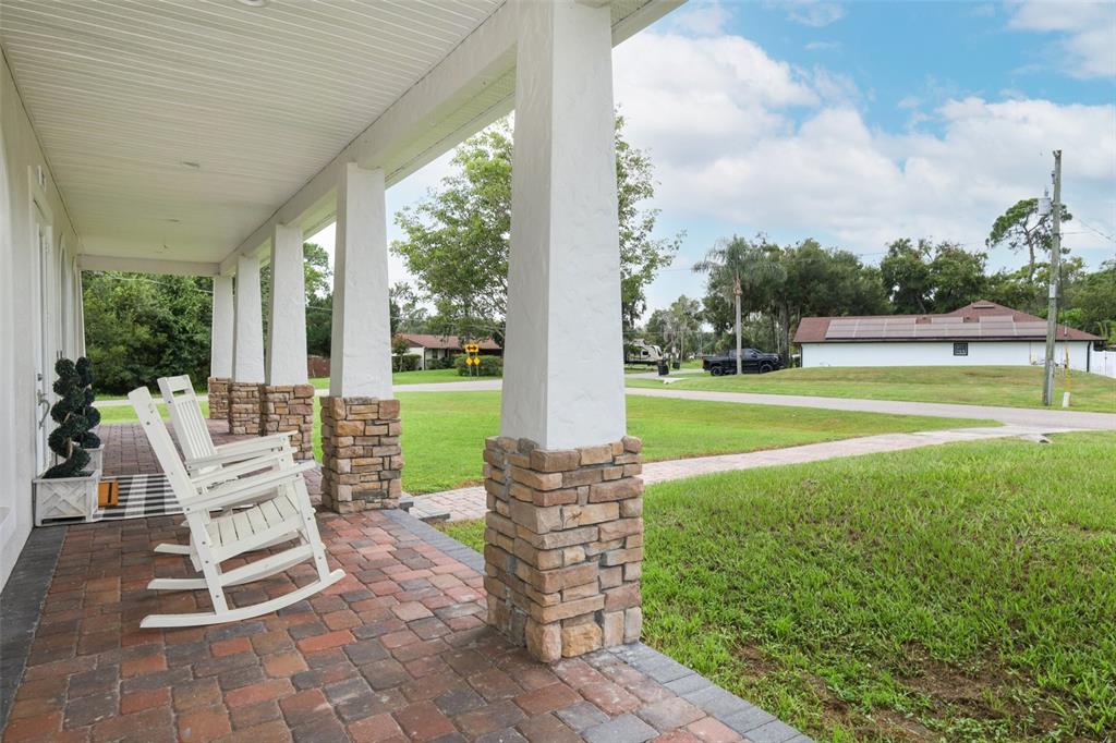 A covered porch features stone-based columns, brick pavers, and white rocking chairs overlooking a yard — 787 FANTASY LANE, CHULUOTA, FL