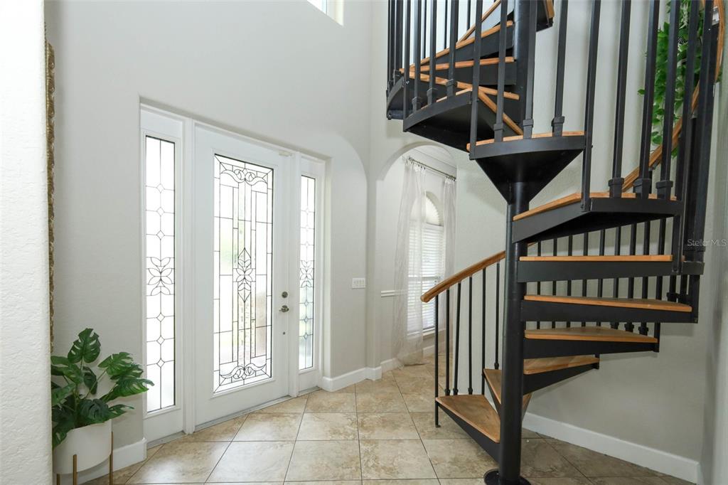 An entryway features tile flooring, a decorative glass front door, and a black spiral staircase — 787 FANTASY LANE, CHULUOTA, FL