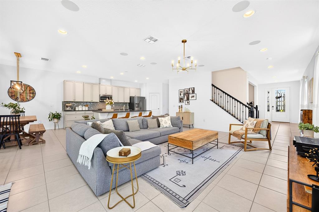 An open-concept living room and kitchen featuring tile floors, a gray sectional, and a staircase — 8205 BAYLISS COURT, ORLANDO, FL