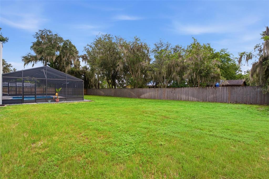 A large grassy backyard features a screened-in swimming pool and a wooden privacy fence — 5240 ROYAL OAK DRIVE, FRUITLAND PARK, FL