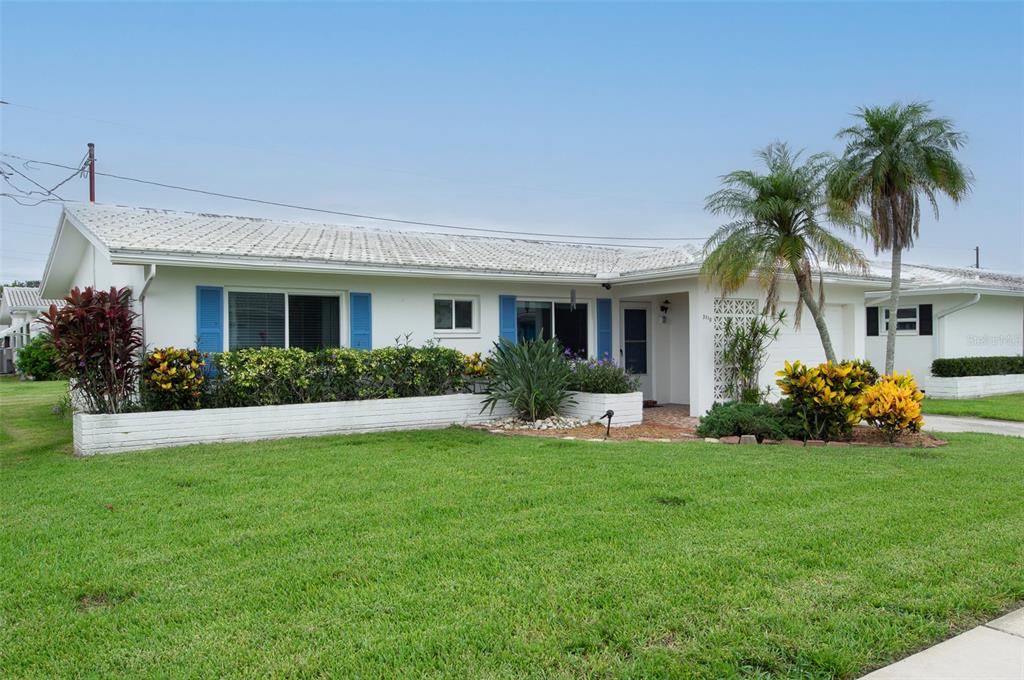 A single-story white house with blue shutters, a low-walled garden, and two palm trees — 3710 98TH AVENUE N, PINELLAS PARK, FL
