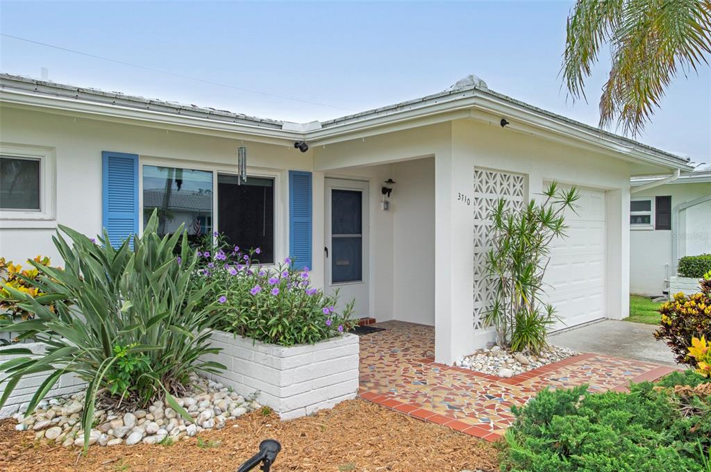 The exterior of a white house features blue shutters, a mosaic tiled porch, and landscaping — 3710 98TH AVENUE N, PINELLAS PARK, FL