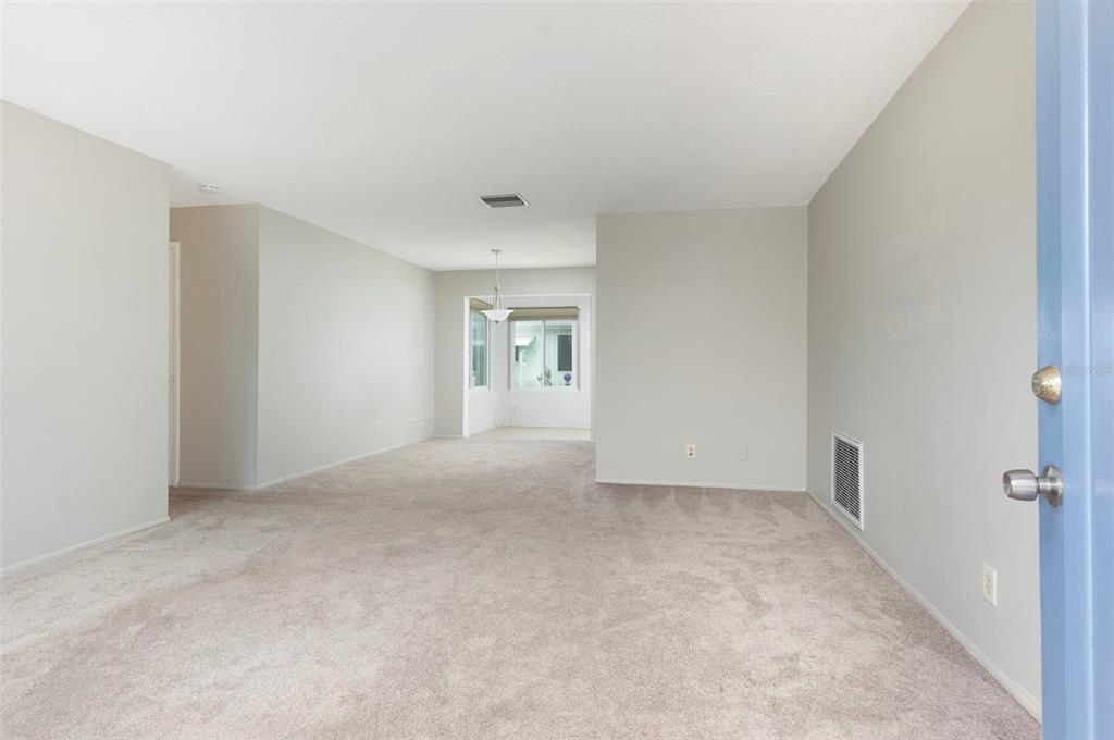 An empty living room with beige carpet, light gray walls, and a view of a dining area — 3710 98TH AVENUE N, PINELLAS PARK, FL