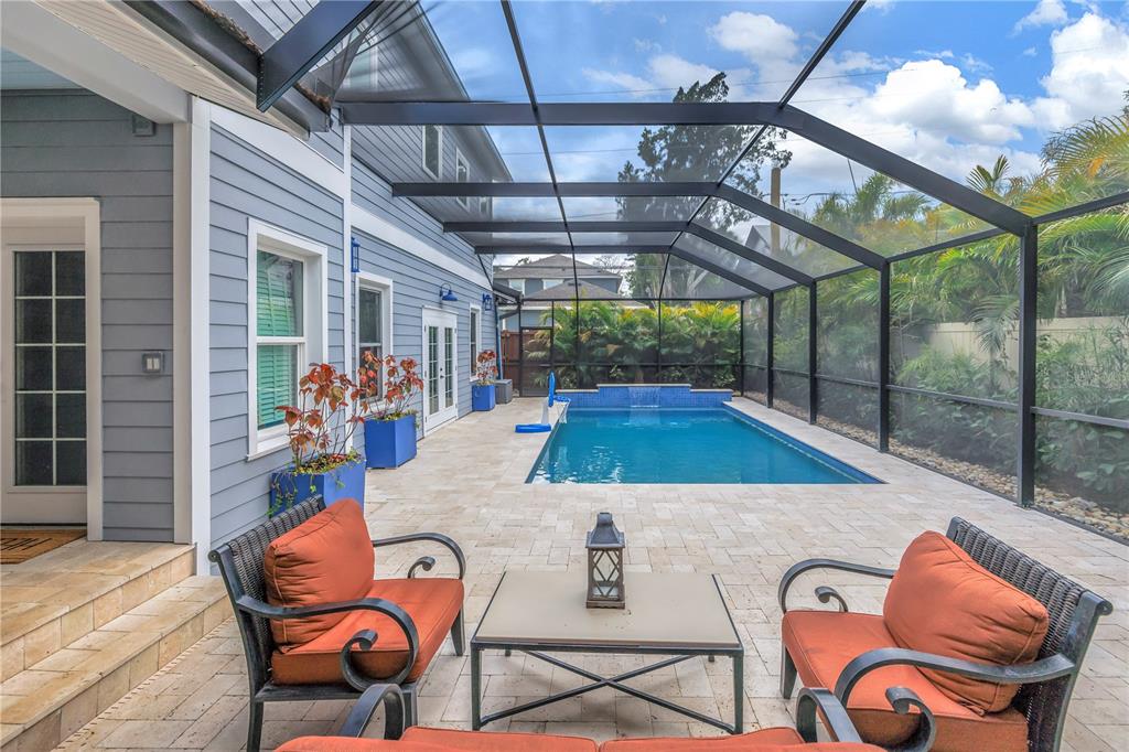 A screened-in patio features a rectangular swimming pool, stone pavers, and outdoor seating furniture — 436 12TH AVENUE NE, ST PETERSBURG, FL