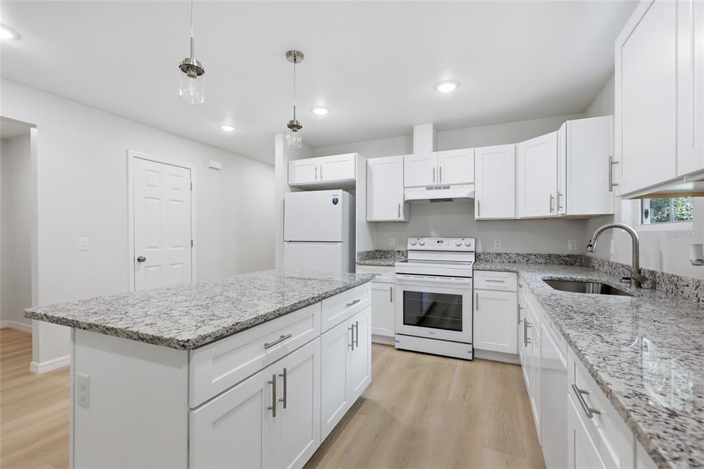 A kitchen features white cabinets, granite countertops, a kitchen island, and white appliances — 925 NE 19TH STREET, GAINESVILLE, FL