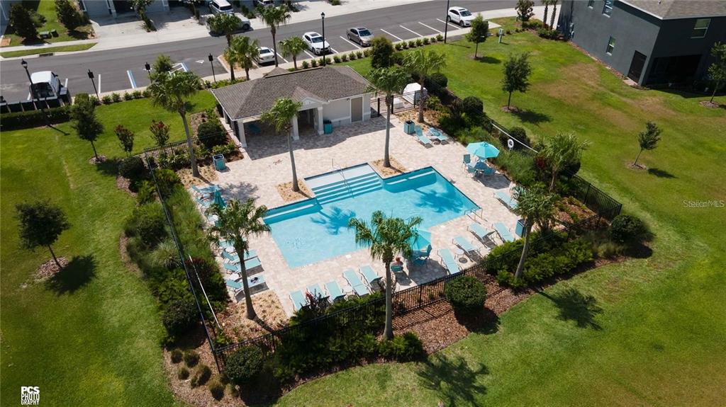 An aerial view shows a community swimming pool with a clubhouse and surrounding lounge chairs — 7926 PENROSE PLACE, WILDWOOD, FL