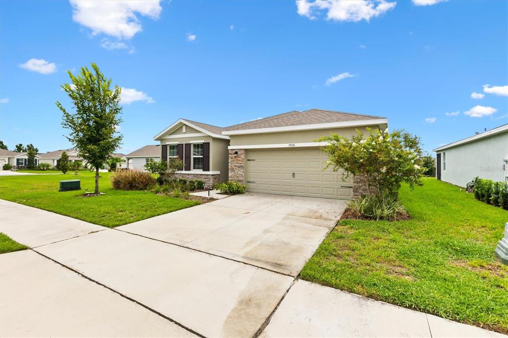 A single-story house with a beige exterior, stone accents, and a two-car garage — 7926 PENROSE PLACE, WILDWOOD, FL