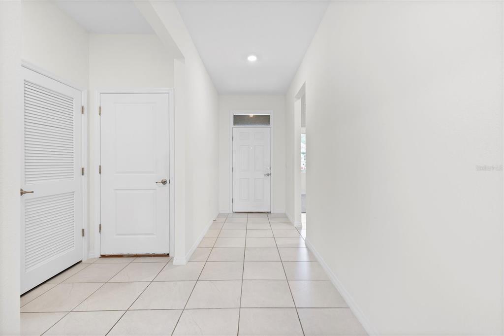 A bright hallway features white walls, tiled flooring, and several closed white doors — 7926 PENROSE PLACE, WILDWOOD, FL