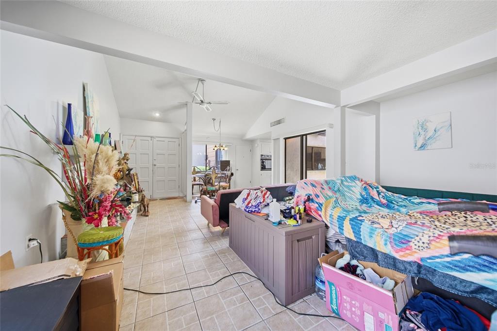 A living room with tiled floors, a vaulted ceiling, and a large bed covered in blankets — 12229 CIDER MILL LANE, HUDSON, FL