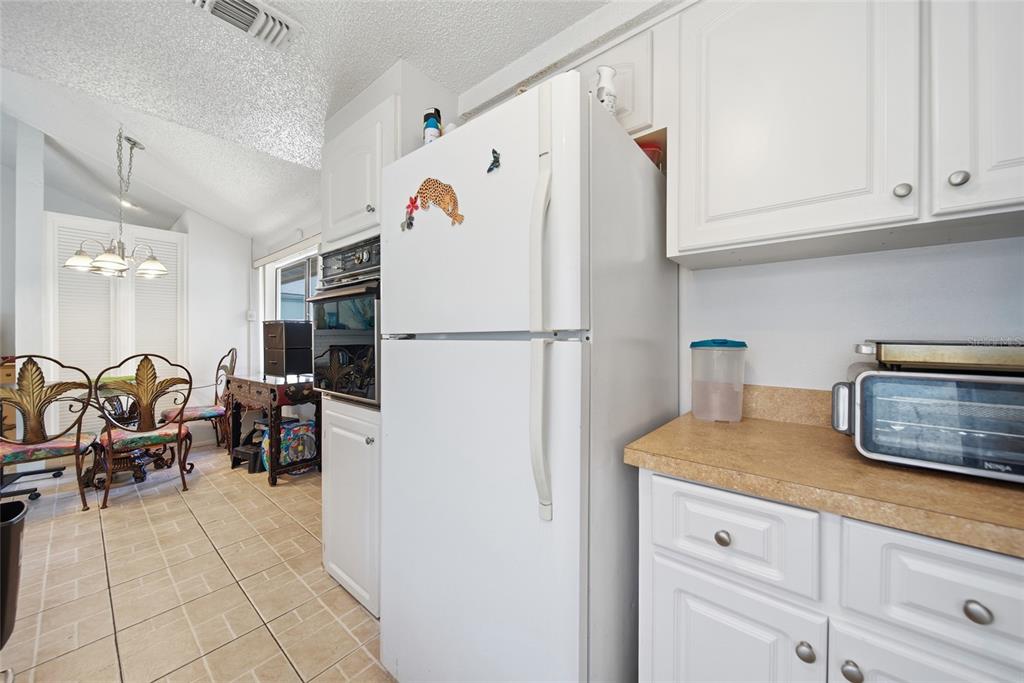 A white kitchen features a refrigerator, wall oven, and a dining area with decorative chairs — 12229 CIDER MILL LANE, HUDSON, FL
