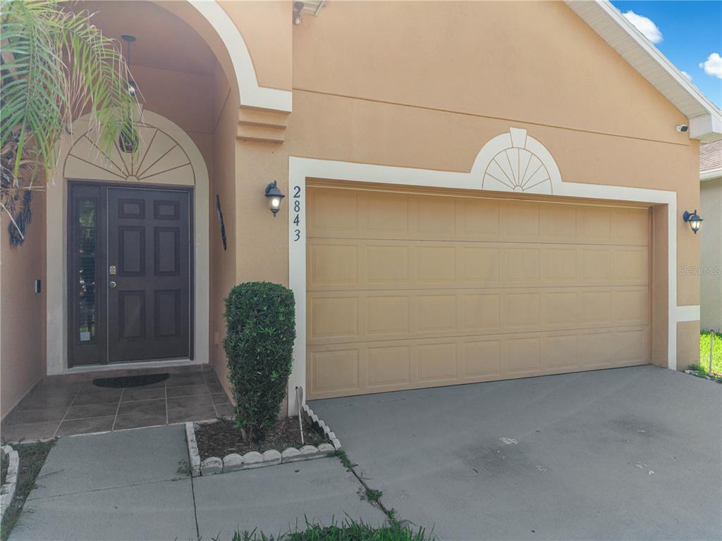 The exterior of a house features a tan stucco facade, a garage, and a front entrance — 2843 JASPER RUN, KISSIMMEE, FL