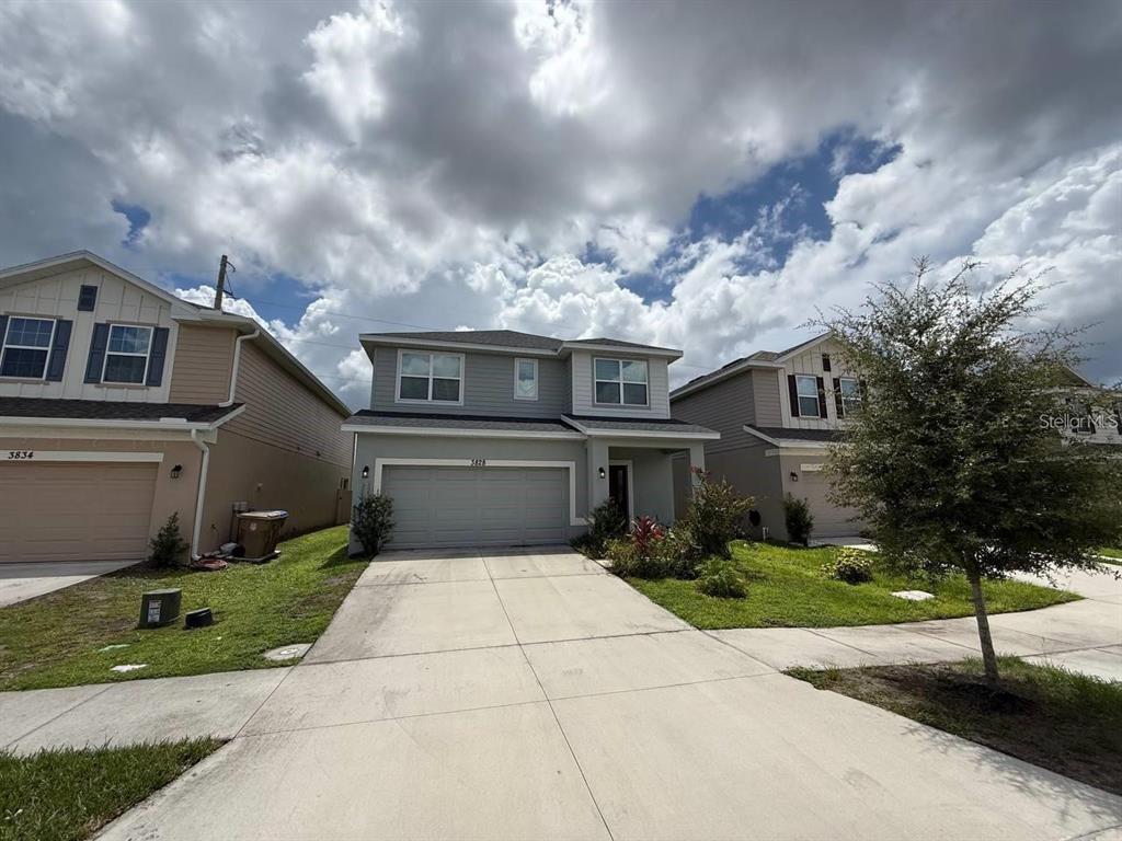 A two-story suburban house with a gray exterior, a two-car garage, and a concrete driveway — 3828 SAGEFIELD DRIVE, HARMONY, FL