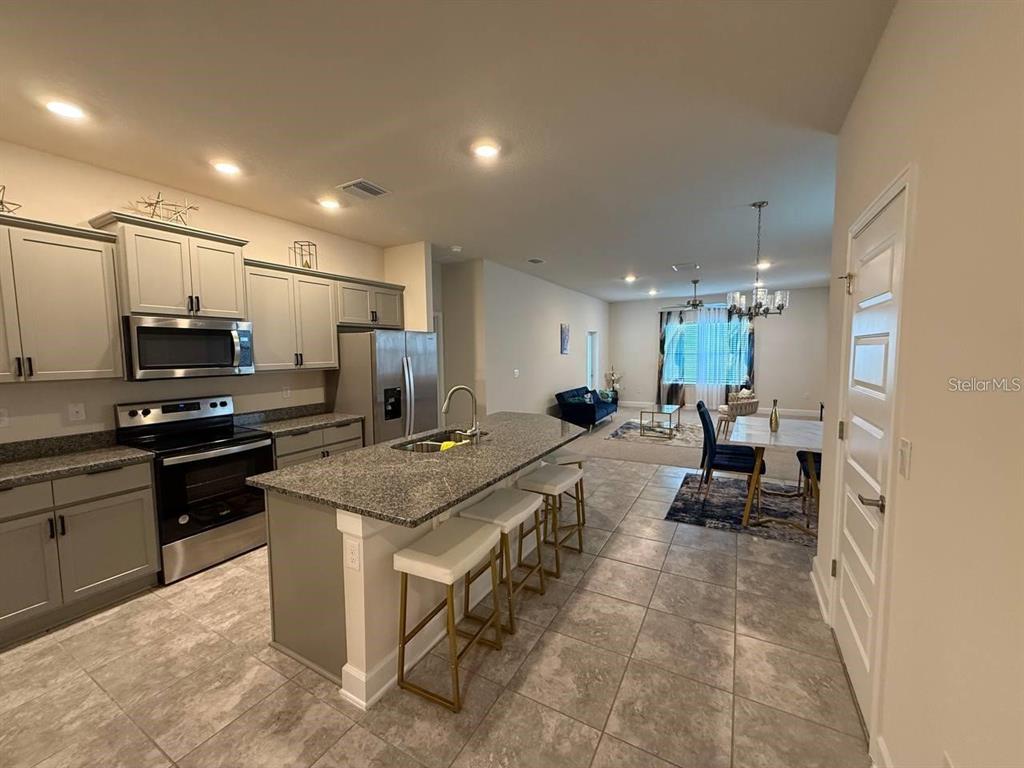 A kitchen with gray cabinets and a granite island overlooks an open-concept dining and living area — 3828 SAGEFIELD DRIVE, HARMONY, FL