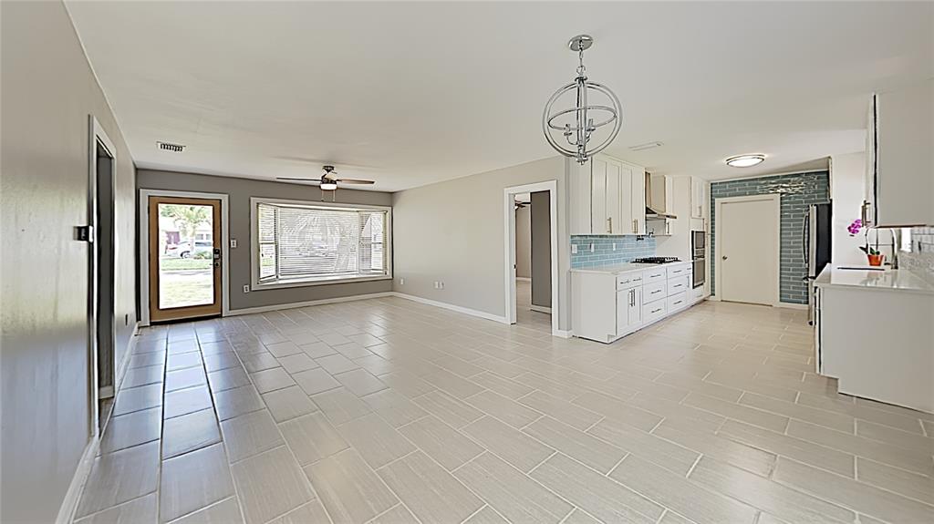 An open-concept kitchen and living area with light tile flooring, white cabinets, and a chandelier — 4511 S GAINES ROAD, TAMPA, FL