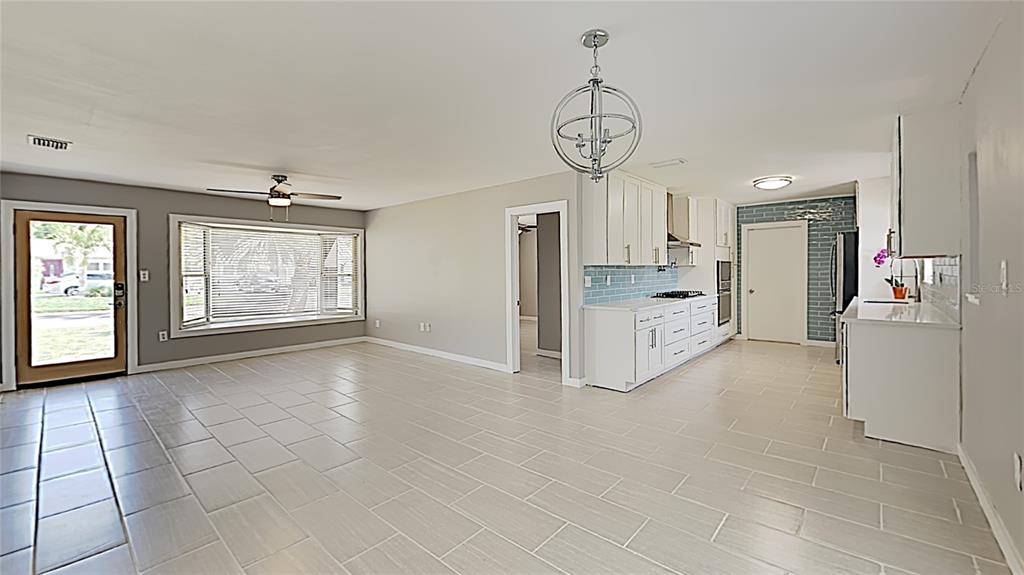 An open-concept living and kitchen area features light tile flooring, white cabinetry, and a chandelier — 4511 S GAINES ROAD, TAMPA, FL