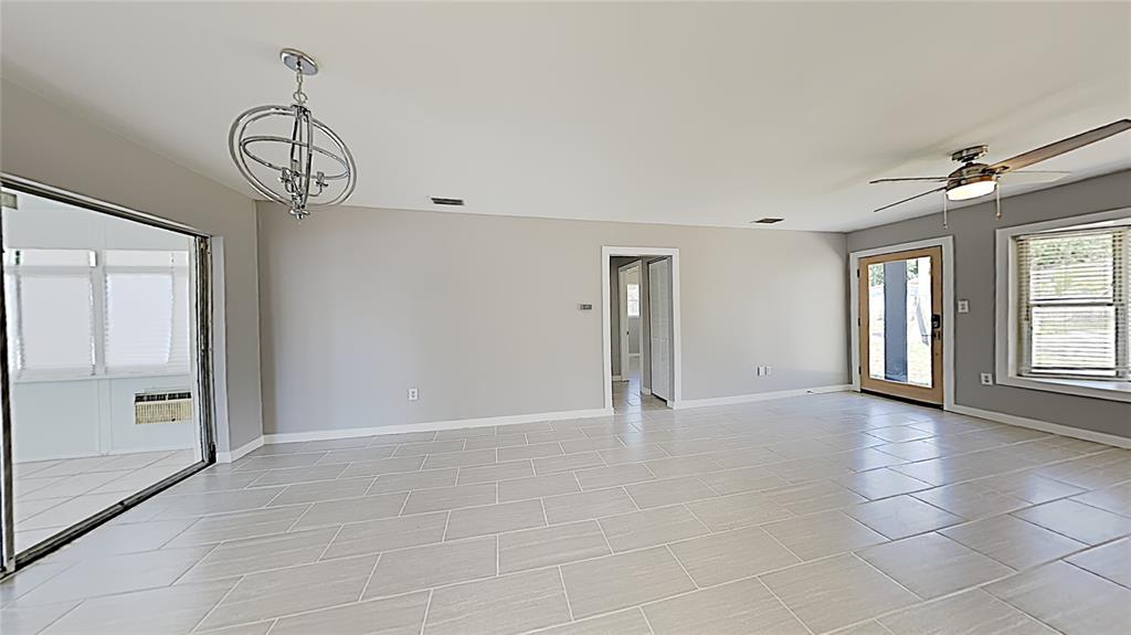 A bright living room features light gray walls, large floor tiles, a chandelier, and ceiling fan — 4511 S GAINES ROAD, TAMPA, FL