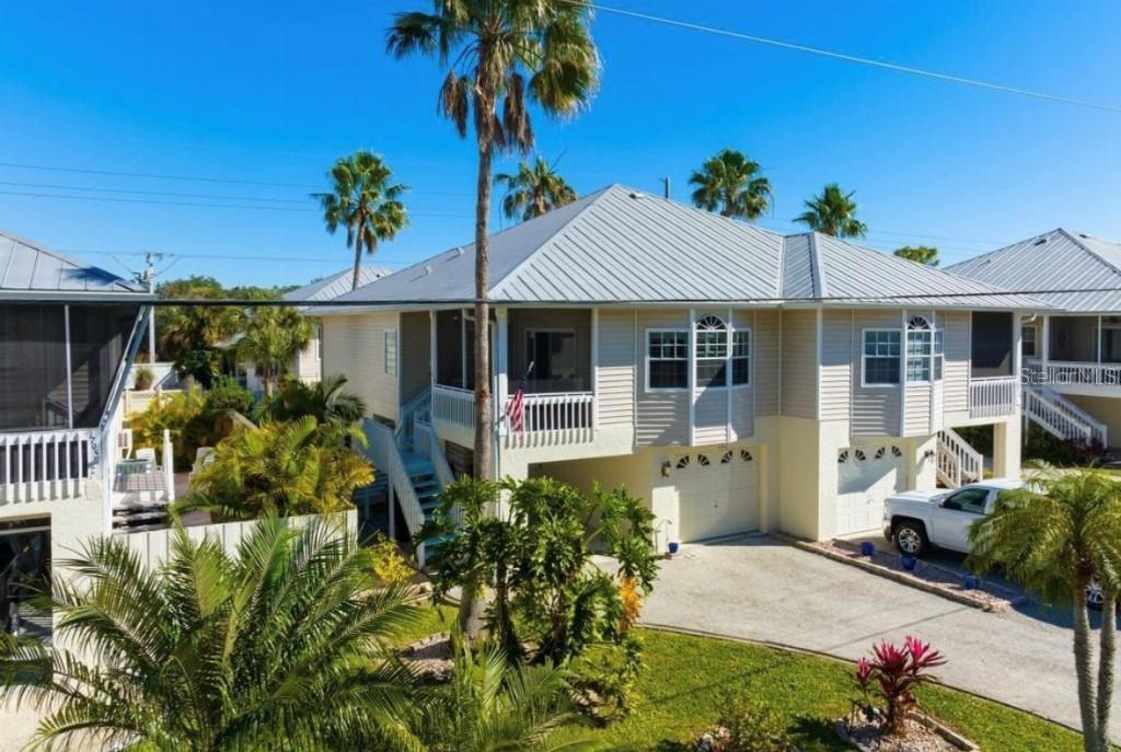 An elevated two-story house with a metal roof, light siding, and a concrete driveway — 1811 HIGHLAND ROAD, OSPREY, FL
