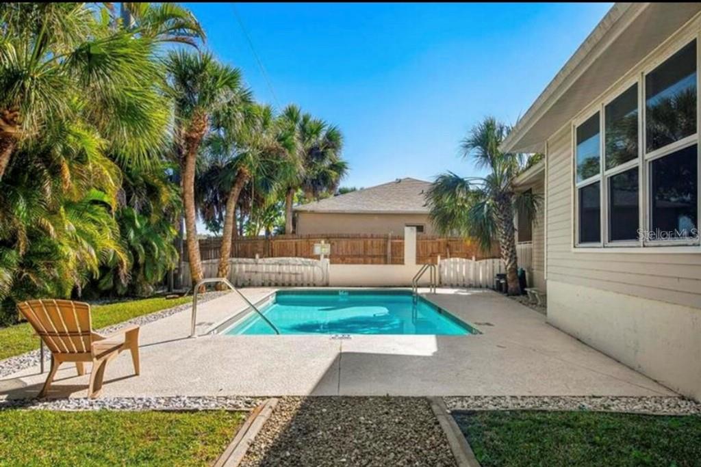 A backyard features a rectangular swimming pool, a concrete patio, and surrounding palm trees — 1811 HIGHLAND ROAD, OSPREY, FL