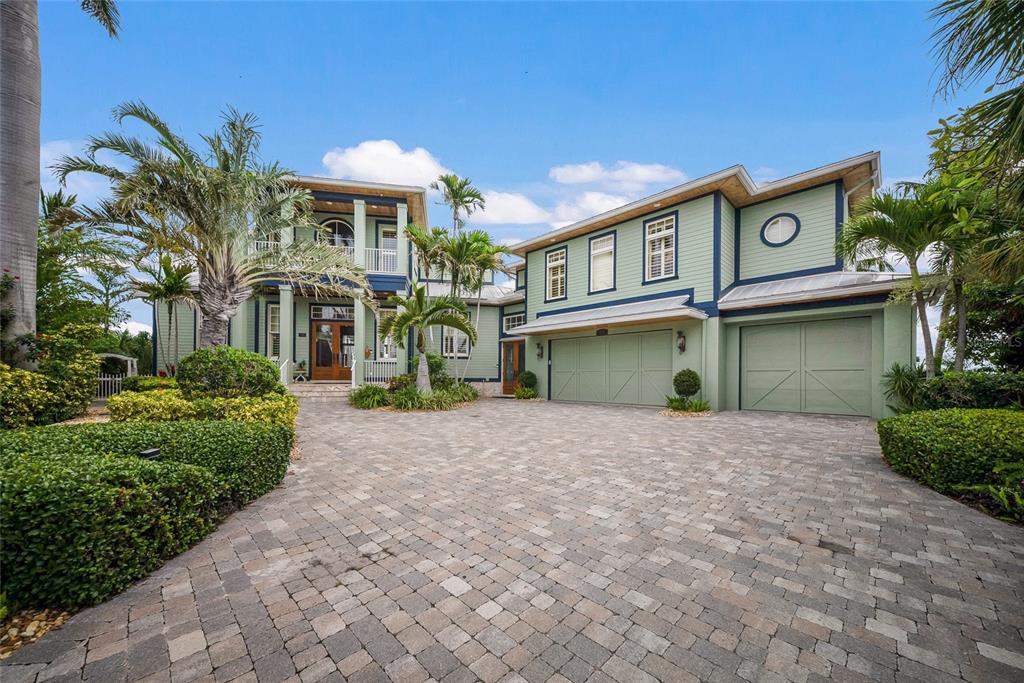 A two-story green house with a paved driveway, palm trees, and a three-car garage — 522 BAYVIEW DRIVE, HOLMES BEACH, FL