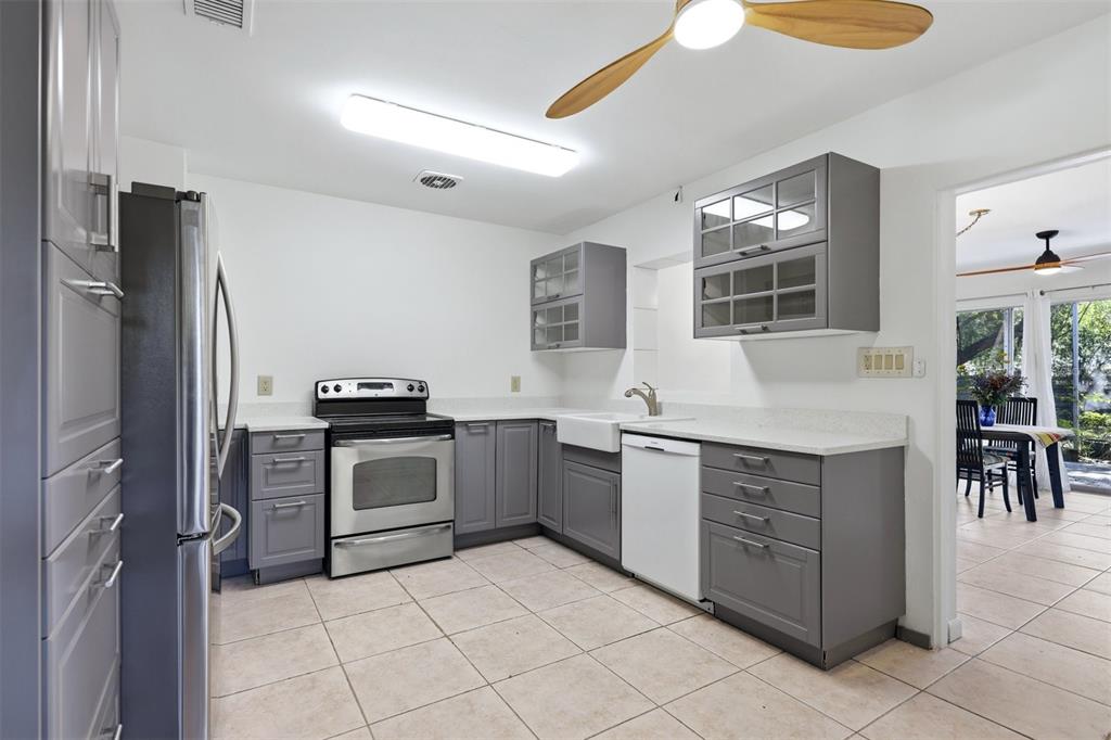 A kitchen features gray cabinets, stainless steel appliances, a white farmhouse sink, and tile flooring — 4003 BOOTH PLACE, SARASOTA, FL