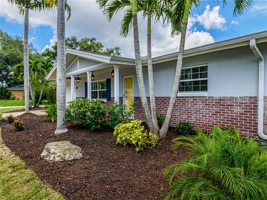 A single-story house with a brick facade, covered porch, and palm trees in the yard — 1661 ALGONQUIN DRIVE, CLEARWATER, FL