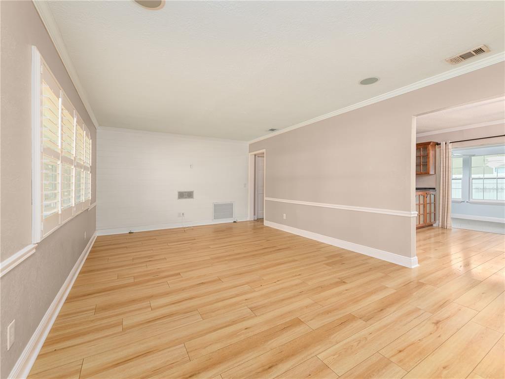An empty living room features light wood-look flooring, beige walls, and white plantation shutters — 1661 ALGONQUIN DRIVE, CLEARWATER, FL